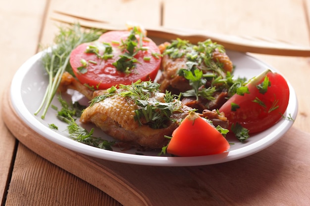 Two golden duck legs with herbs and tomatoes on a white plate on a wooden background Baked duck closeup