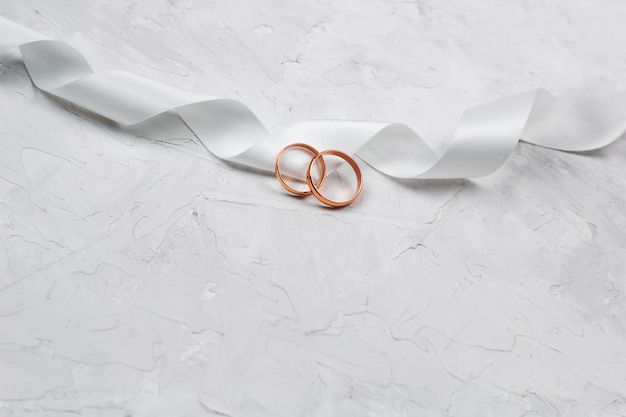 Two golden rings and white satin ribbon wedding decor or wedding invitation background concept