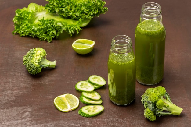 Two green smoothie bottles Slices of cucumber lime broccoli and lettuce on brown