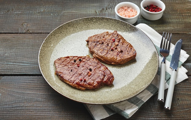 Two grilled ribeye steaks spices and tomatocucumber salad with sour cream on a wooden table