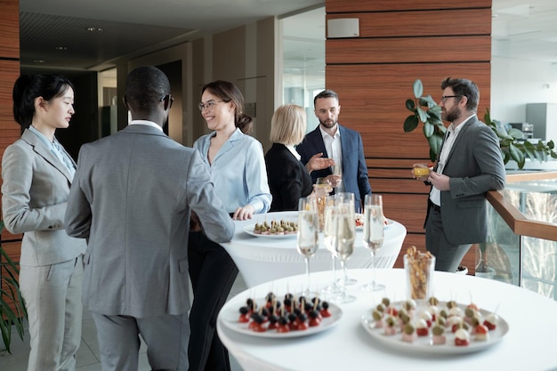 Two groups of successful speakers in formalwear talking by served tables