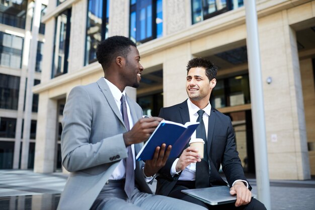 Two guys wearing business suits consulting notepad outdoors