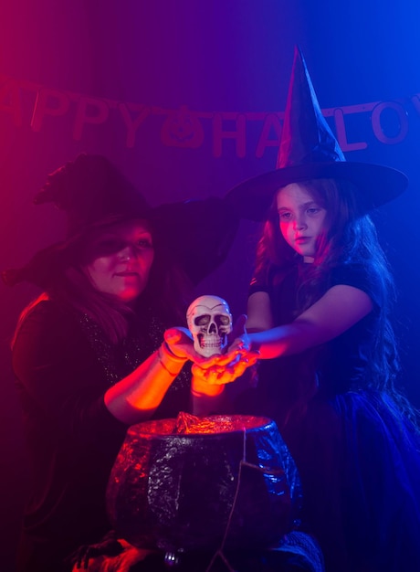 Photo two halloween witches making a potion and conjure with skull in halloween night magic holidays and mystic concept