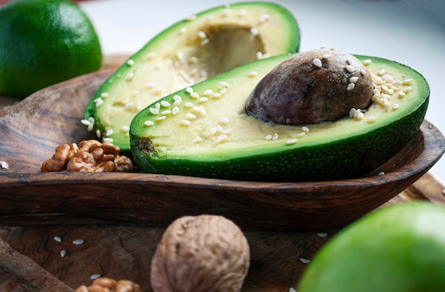 Two halves of avocado on a wooden plate sprinkled with sesame near walnuts, apple and lime.