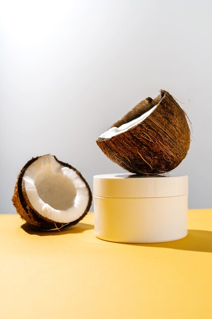 Photo two halves of coconut and a jar of cosmetics on a yellow and gray background