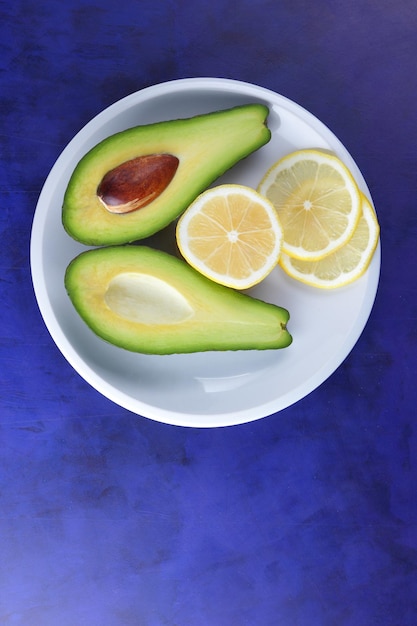 Two halves of a ripe avocado with seed on a white plate Closeup green healthy fruit with citrus on a blue background