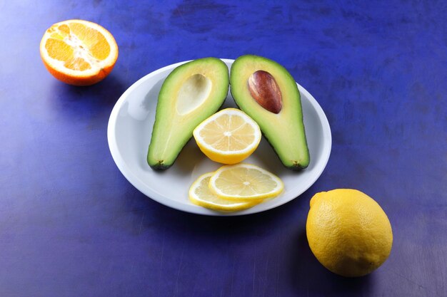 Two halves of a ripe avocado with seed on a white plate Closeup green healthy fruit with citrus on a blue background