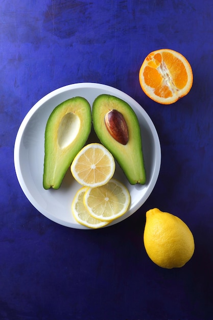 Two halves of a ripe avocado with seed on a white plate Closeup green healthy fruit with citrus on a blue background