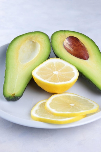 Two halves of a ripe avocado with seed on a white plate Green healthy fruit with lemon slices isolated on white background Vegetarian food concept Closeup