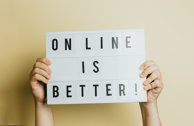 Two hands holding a sign that says online is better over a pastel yellow background, styling and design concept, copy space, buy online and e-commerce