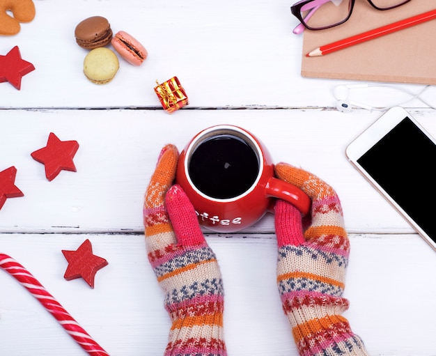 Photo two hands in knitted mittens hold a red cup with  coffee