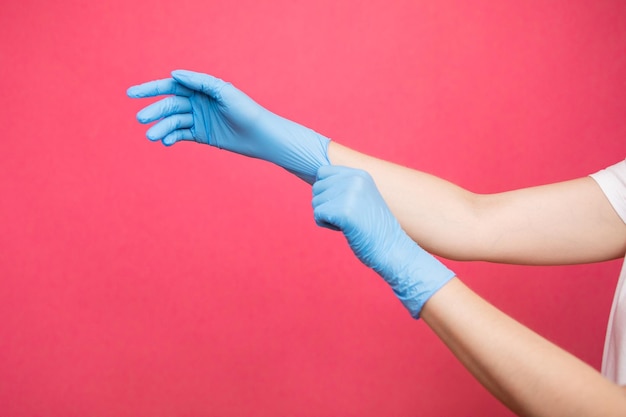 Two hands of a woman wearing nitrile gloves on a pink background