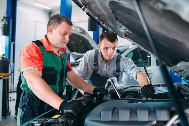 Two handsome mechanics in uniform are working in auto service. Car repair and maintenance.