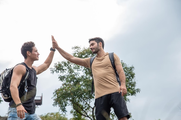 Two handsome men touch their hands while standing on a rock during a trekking tour