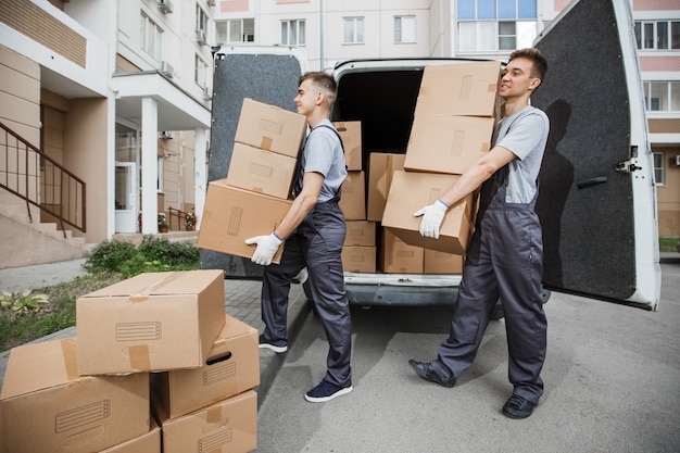 Photo two handsome workers wearing uniforms are unloading the van full of boxes