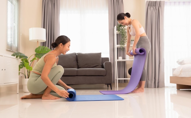 Two happiness young yoga women rolling mat after doing yoga exercise workout in living room at home Healthy life and fitness training workout concept