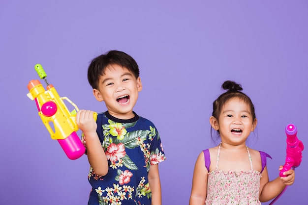 Two Happy Asian little boy and girl holding plastic water gun, Thai children funny hold toy water pistol and smile,