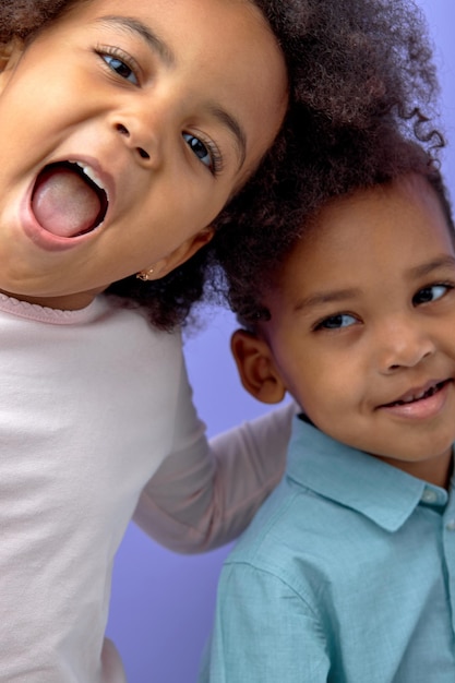 Two happy black children posing at camera and cheerfully smiling over purple studio background cute