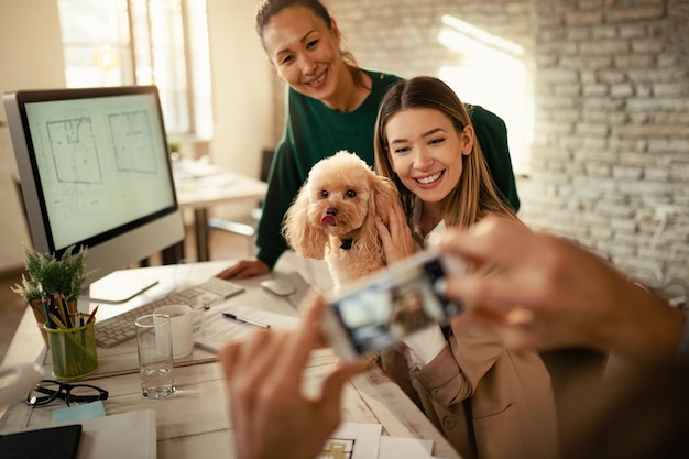 Two happy creative women and their poodle being photographed in the office