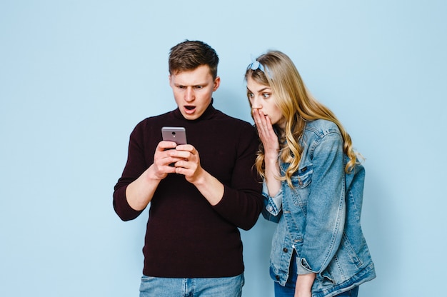 Two happy friends who are excited with phones in their hands isolated on a blue background