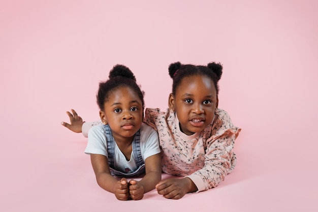 Two happy funny children laughing little African girls in pastel casual clothes lying and posing