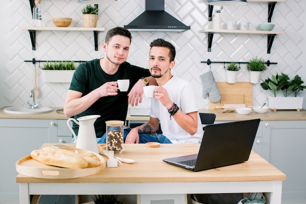 Two happy gay men in homewear spending morning in the kitchen. Happy gay men having breakfast at home in the morning