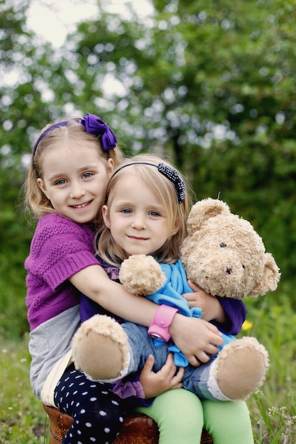 Two happy girls hug teddy bear toy outdoor