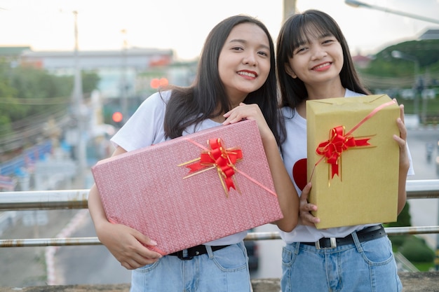 Two happy girls with gift boxes standing with city background.