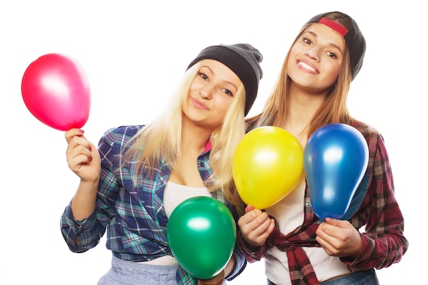 Two happy hipster girls smiling and holding colored balloons over white background