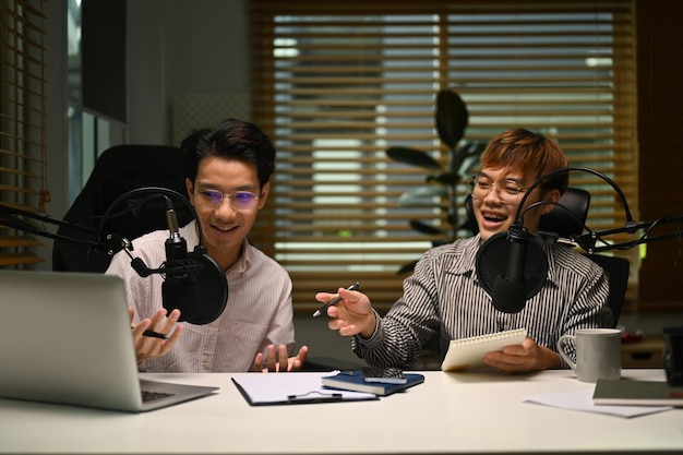 Two happy man using laptop and microphone streaming audio podcast at home studio Entertainment podcasts and technology concept