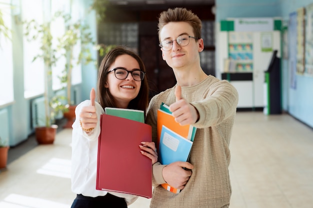 Two happy students in good mood showing thumbs up