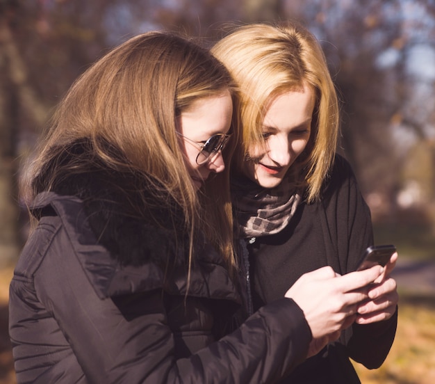 Two happy women friends sharing social media in a smart phone outdoors in a park