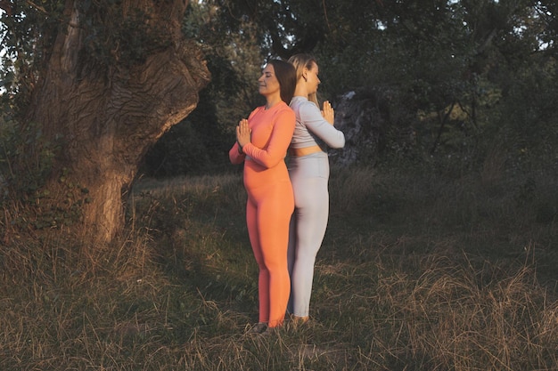 Two happy young girlfriends practice yoga outdoors