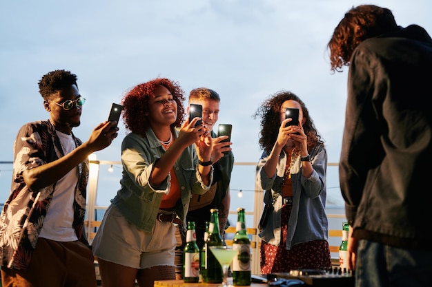 Two happy young intercultural couples taking photo of deejay at rooftop party