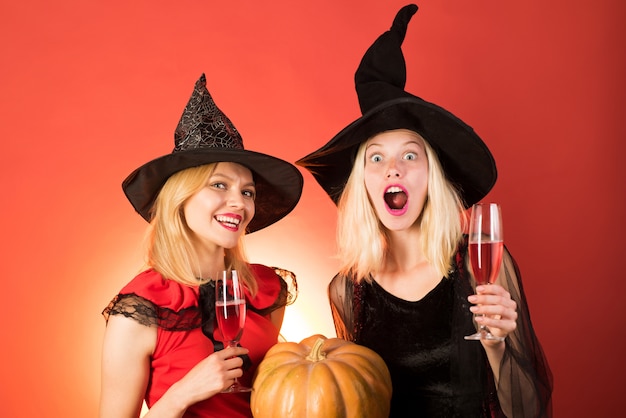 Two happy young woman girls in witches halloween costumes on party over orange wall.