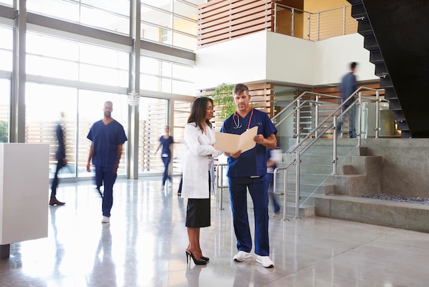 Two healthcare workers talk in the lobby of a busy hospital