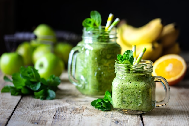 Two healthy green smoothies with spinach, banana, orange, apple, kiwi and mint in glass jar and ingredients. Detox, diet, healthy, vegetarian food concept.