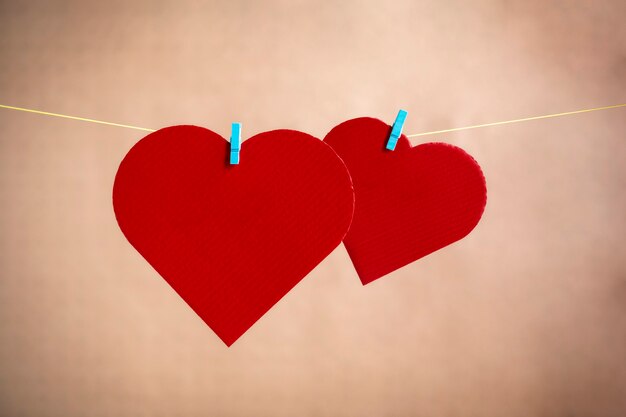 Photo two hearts made of cardboard and painted in red lying on a rope with clamps. valentine's day concept. space for text.