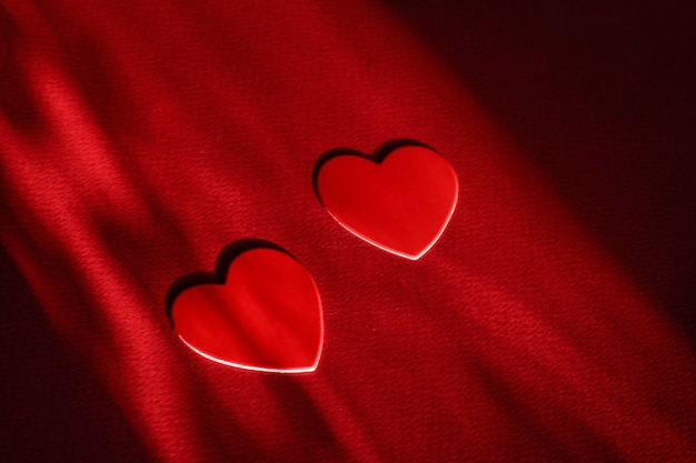 Two hearts on a red background, hard shadows. Valentine's day concept. Copy space