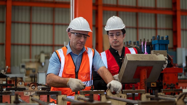 Two Heavy Industry Foreman Engineer ware safety jacket Daily preventive maintenance check machine in Manufacturing Factory use Labtop Have Discussion Training up Skills Maintenance Quality