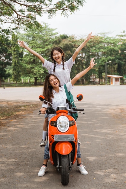 Two high school girls riding motorbikes standing while celebrating graduation