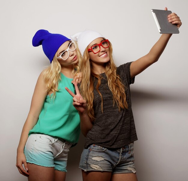 two hipster girls friends taking selfie with digital tablet studio shot over gray vackground