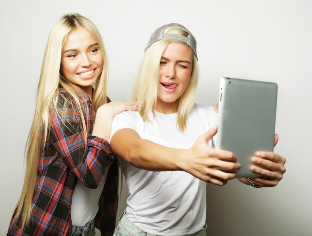 two hipster girls friends taking selfie with digital tablet studio shot over gray vackground