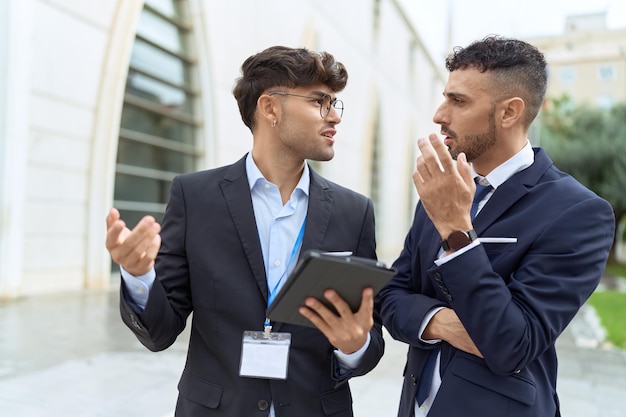 Two hispanic men business workers using touchpad speaking at street