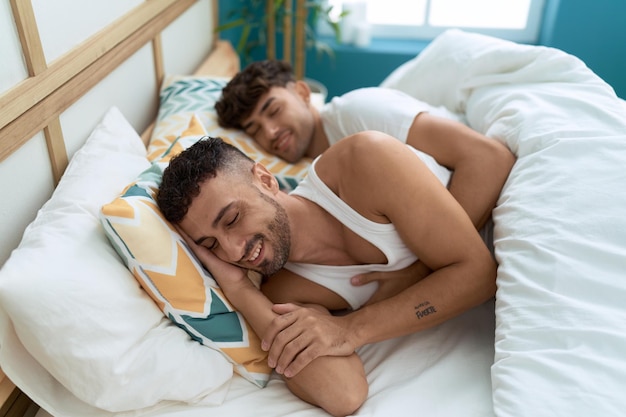 Two hispanic men couple hugging each other lying on bed at bedroom