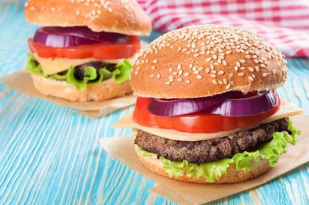 Two homemade cheeseburgers with beef patties and fresh salad on seasame buns, sered on blue wooden table.