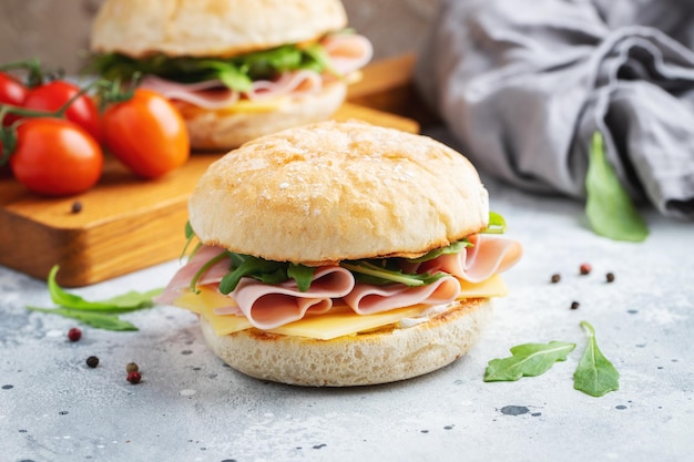 Two homemade sandwiches with ham cheese and arugula on a concrete table