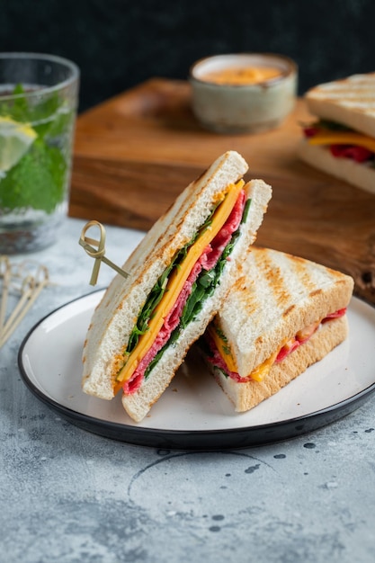 Two homemade sandwiches with sausage cheese and arugula on a light concrete background