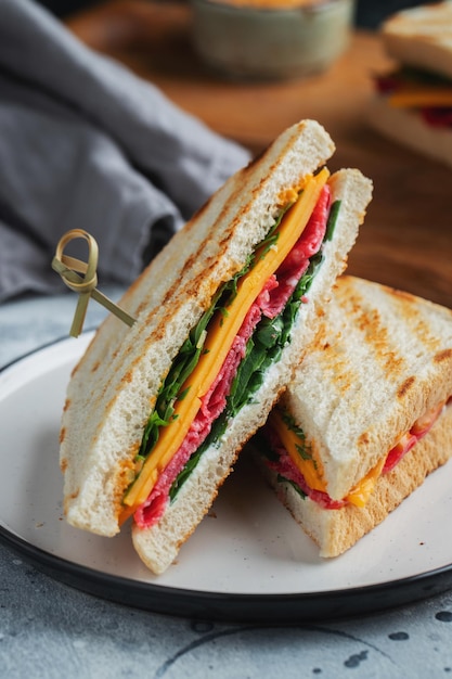 Two homemade sandwiches with sausage cheese and arugula on a light concrete background