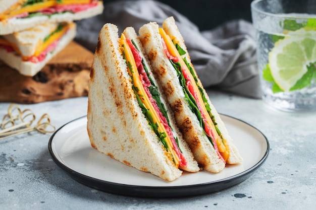 Two homemade sandwiches with sausage cheese and arugula on a light concrete background